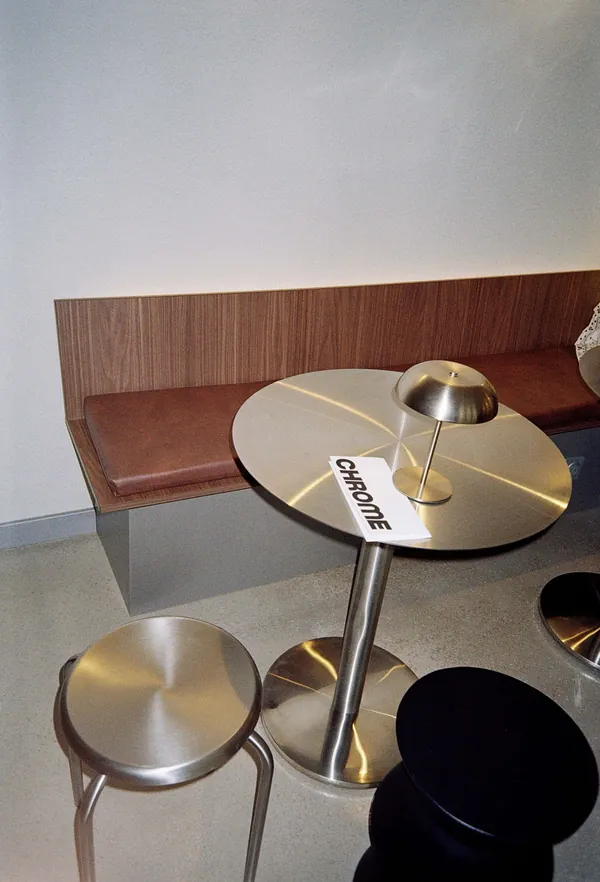 Table ronde en inox, lampe champignon et tabourets dans la salle de Chrome Coffee