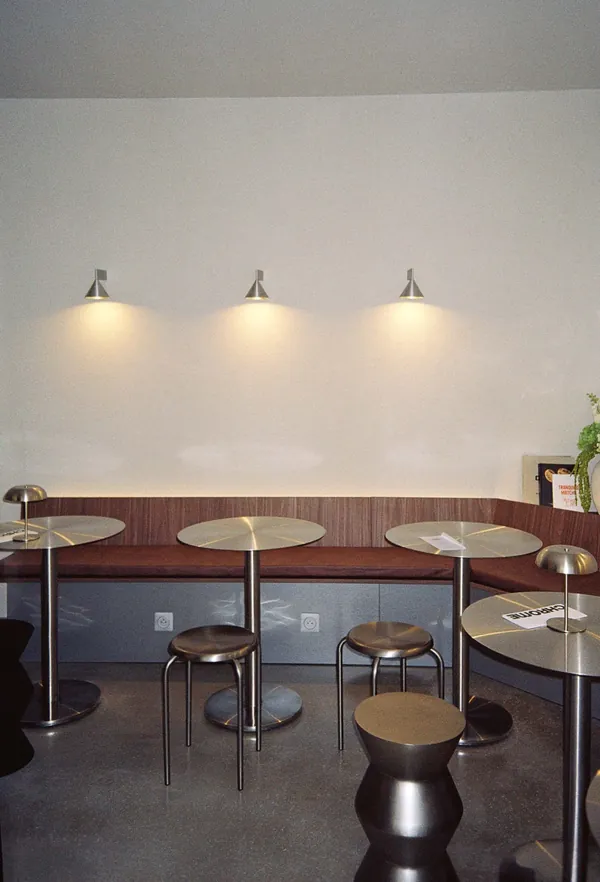 Banquette en bois et tables rondes éclairées par des appliques murales