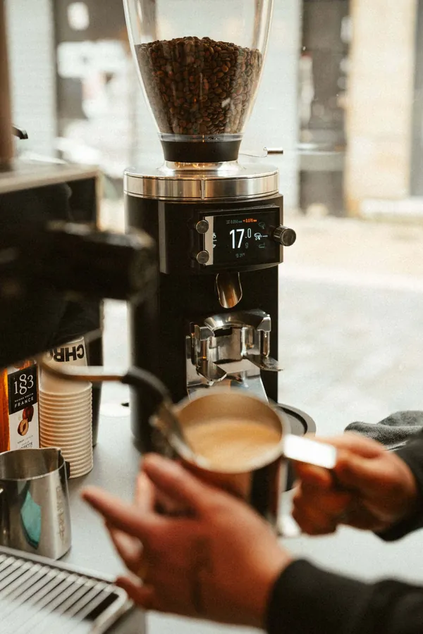 Barista tenant un pichet de lait devant le moulin à café