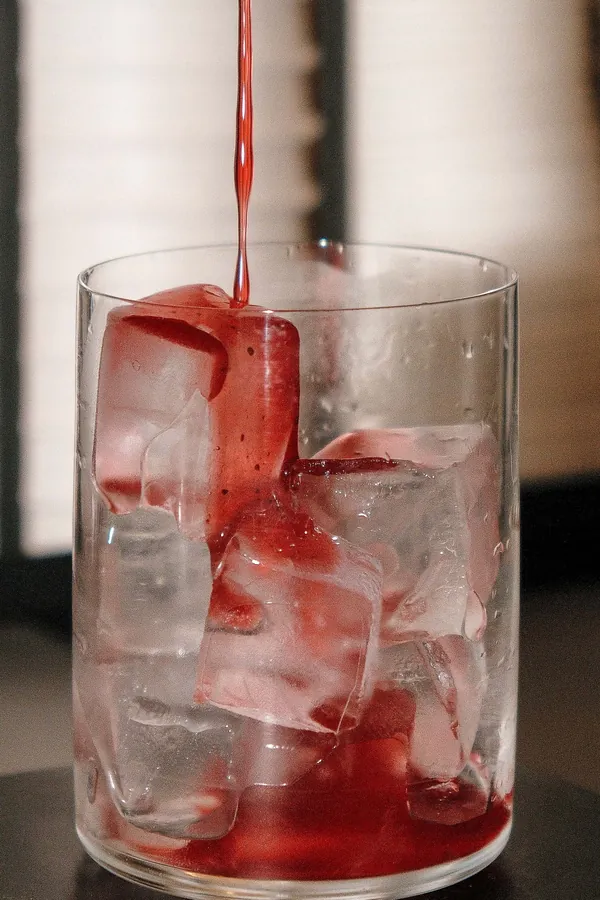 Sirop rouge versé dans un verre rempli de glaçons